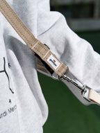 Beige dog leash attached to a gray hoodie with a blurred green background